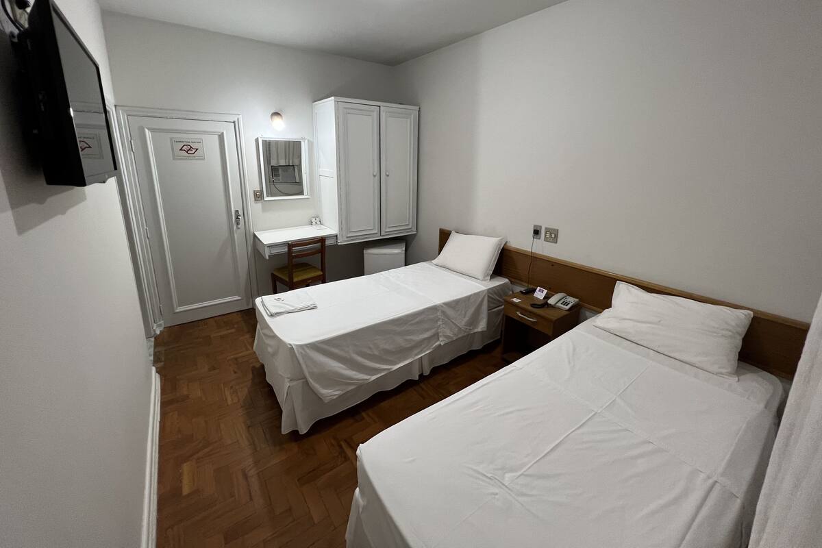 A hotel room with two beds, a desk, a chair, a wardrobe, and a TV.