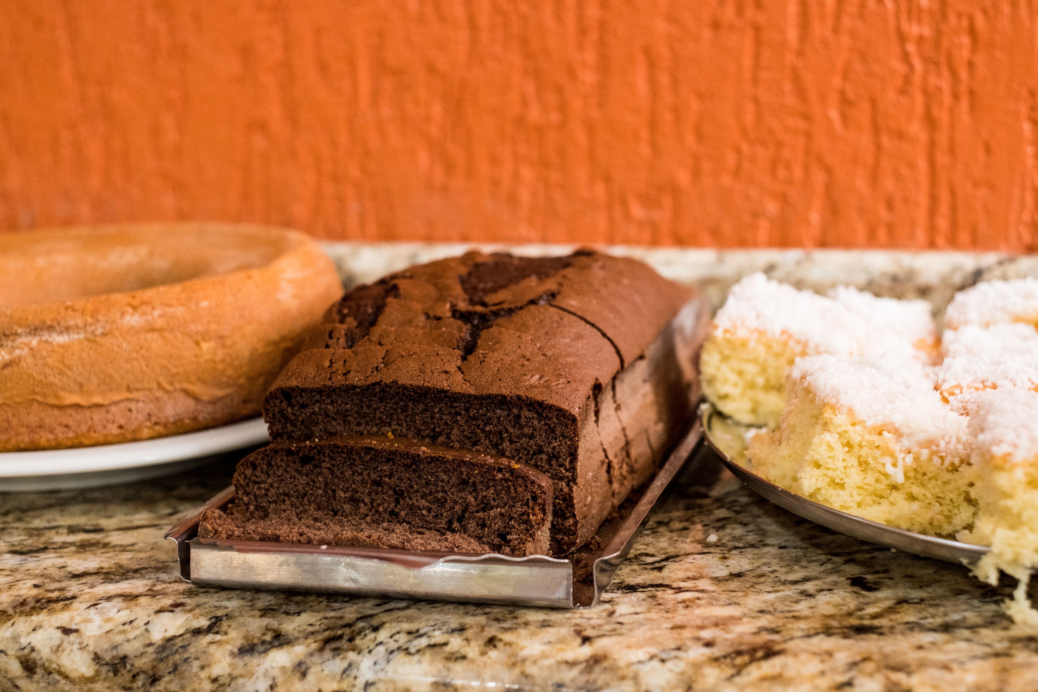 A loaf of chocolate cake, a bundt cake, and a cake with white frosting on a marble countertop.