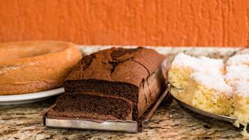 A loaf of chocolate cake, a bundt cake, and a cake with white frosting on a marble countertop.