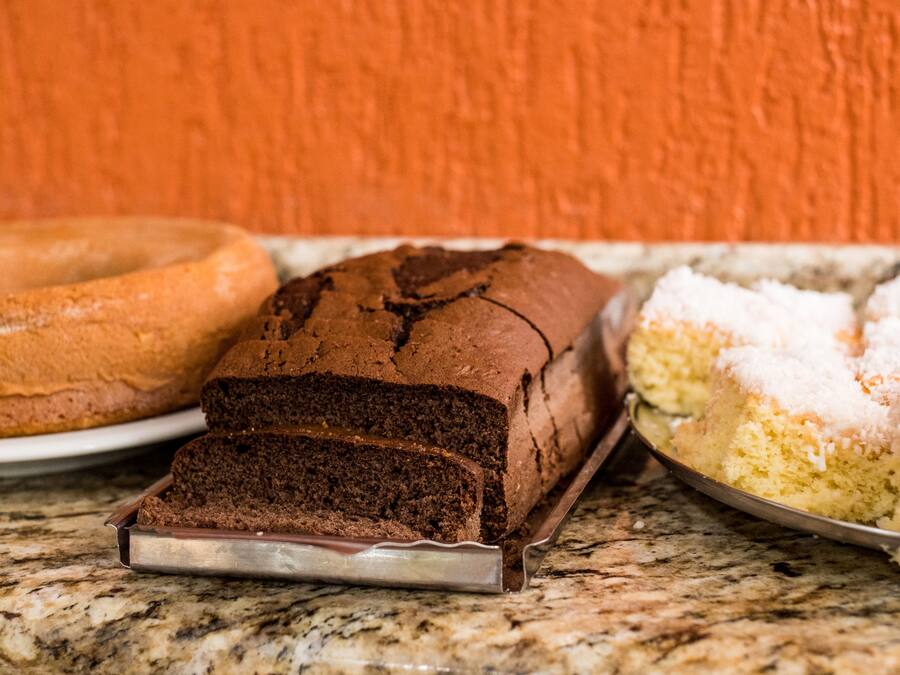 A loaf of chocolate cake, a bundt cake, and a cake with white frosting on a marble countertop.
