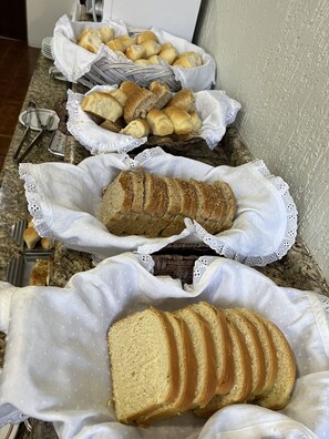 A buffet table with various bread items, including rolls and sliced bread with peanut butter.