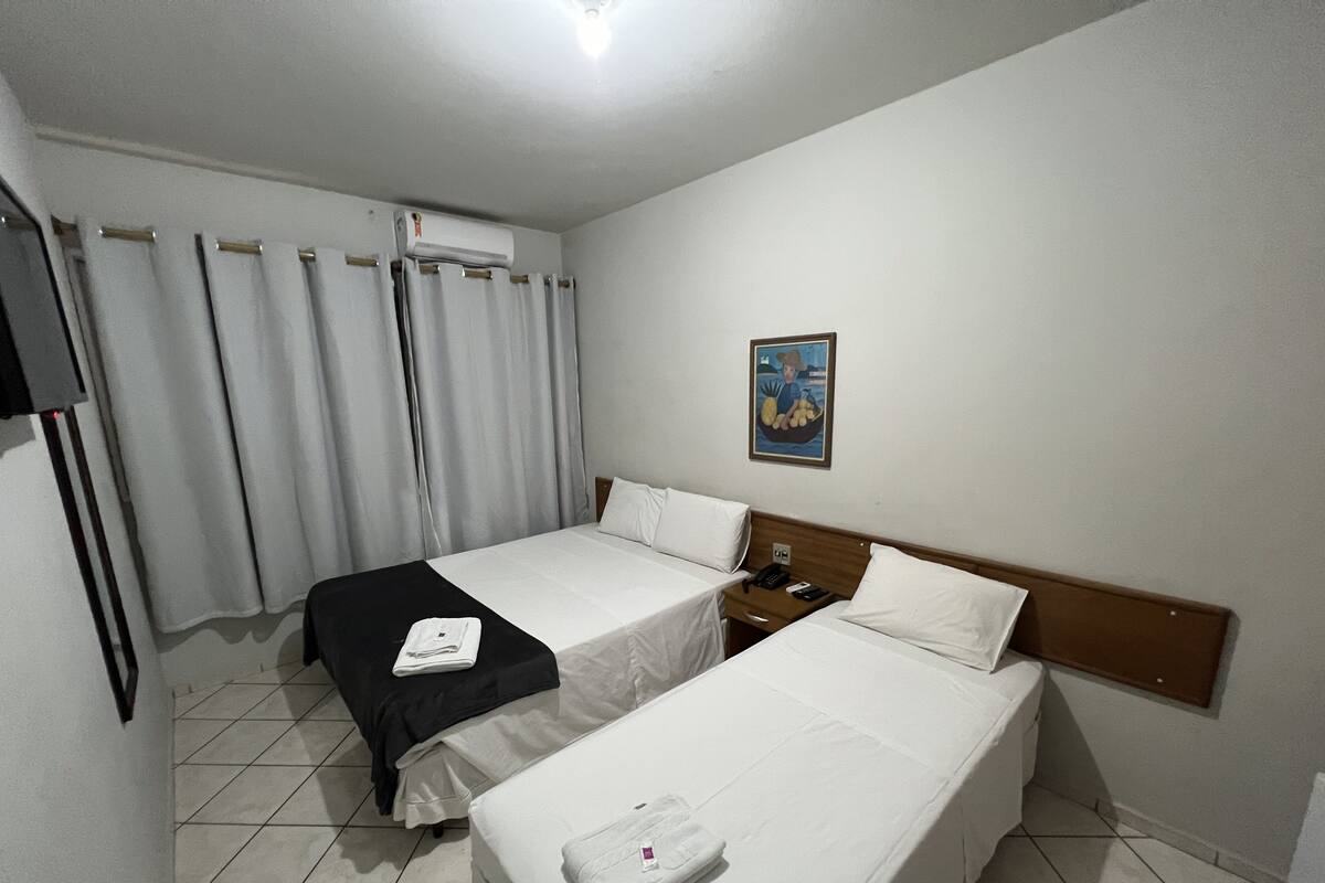 A hotel room with two beds, a nightstand, a telephone, and a painting on the wall.