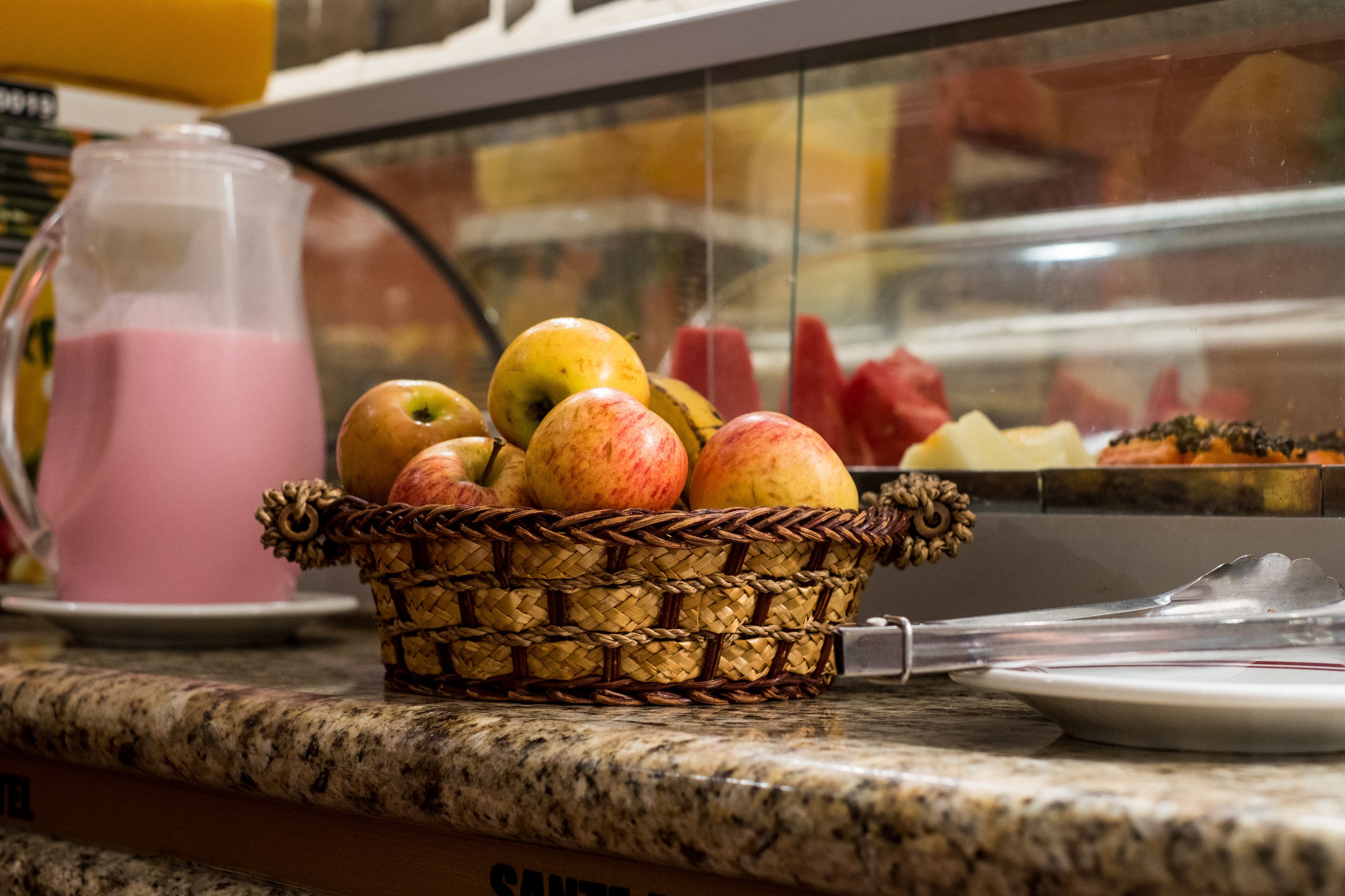 A basket of apples and a pink drink on a granite countertop.
