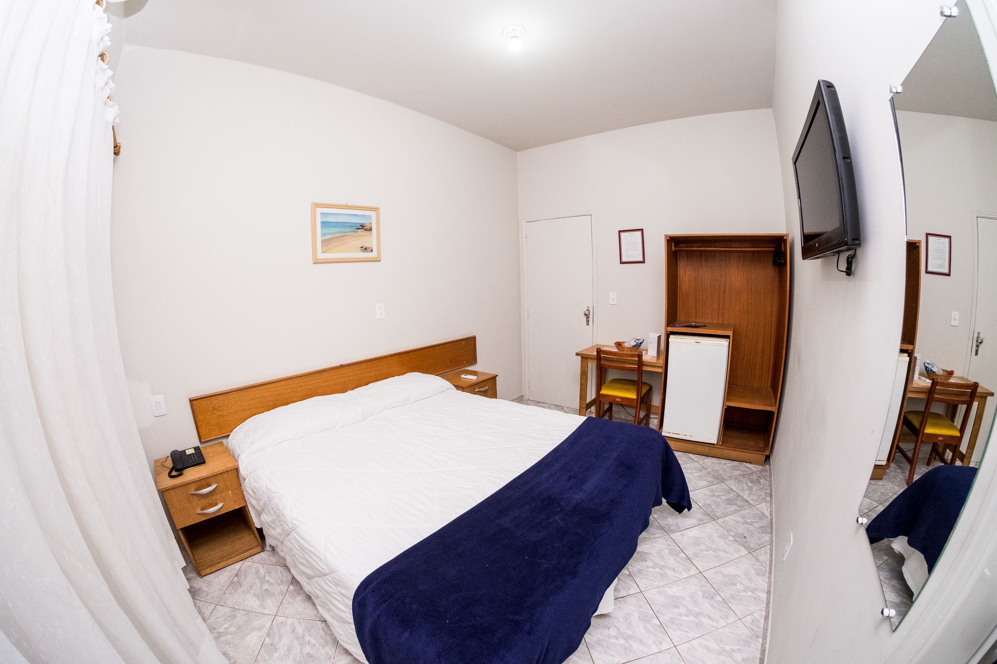A hotel room with a bed, a desk, a chair, a TV, and a door.