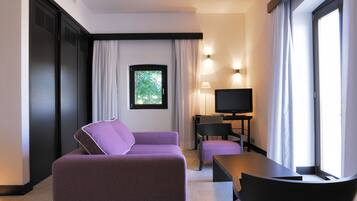 A modern hotel room with a purple sofa, a small table, a TV, and a window with curtains.