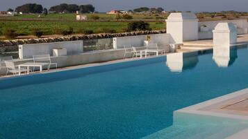 Una piscina con sedie e tavoli bianchi, circondata da un muro in pietra e con vista sulla campagna.