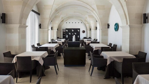 Un restaurante con una barra central, varias mesas y un techo alto abovedado.