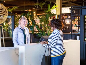 Un espace d’accueil doté d’un comptoir en marbre, de plantes d’intérieur et d’un bar en arrière-plan.