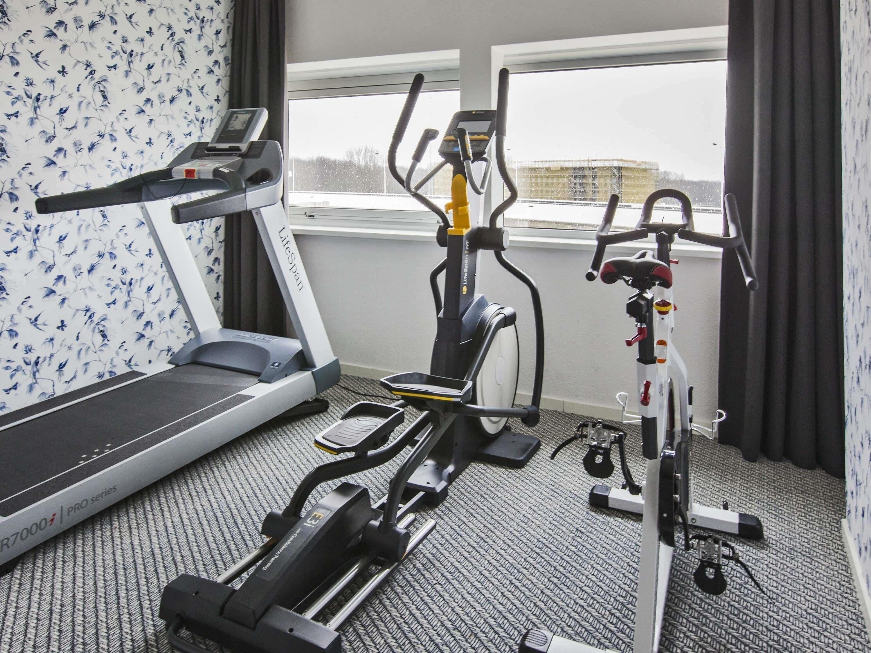 Habitación de hotel con una caminadora, una elíptica y una bicicleta estática.