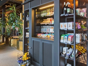 Una tienda con estantes llenos de bebidas embotelladas, bocadillos envasados y una exhibición de productos frescos.