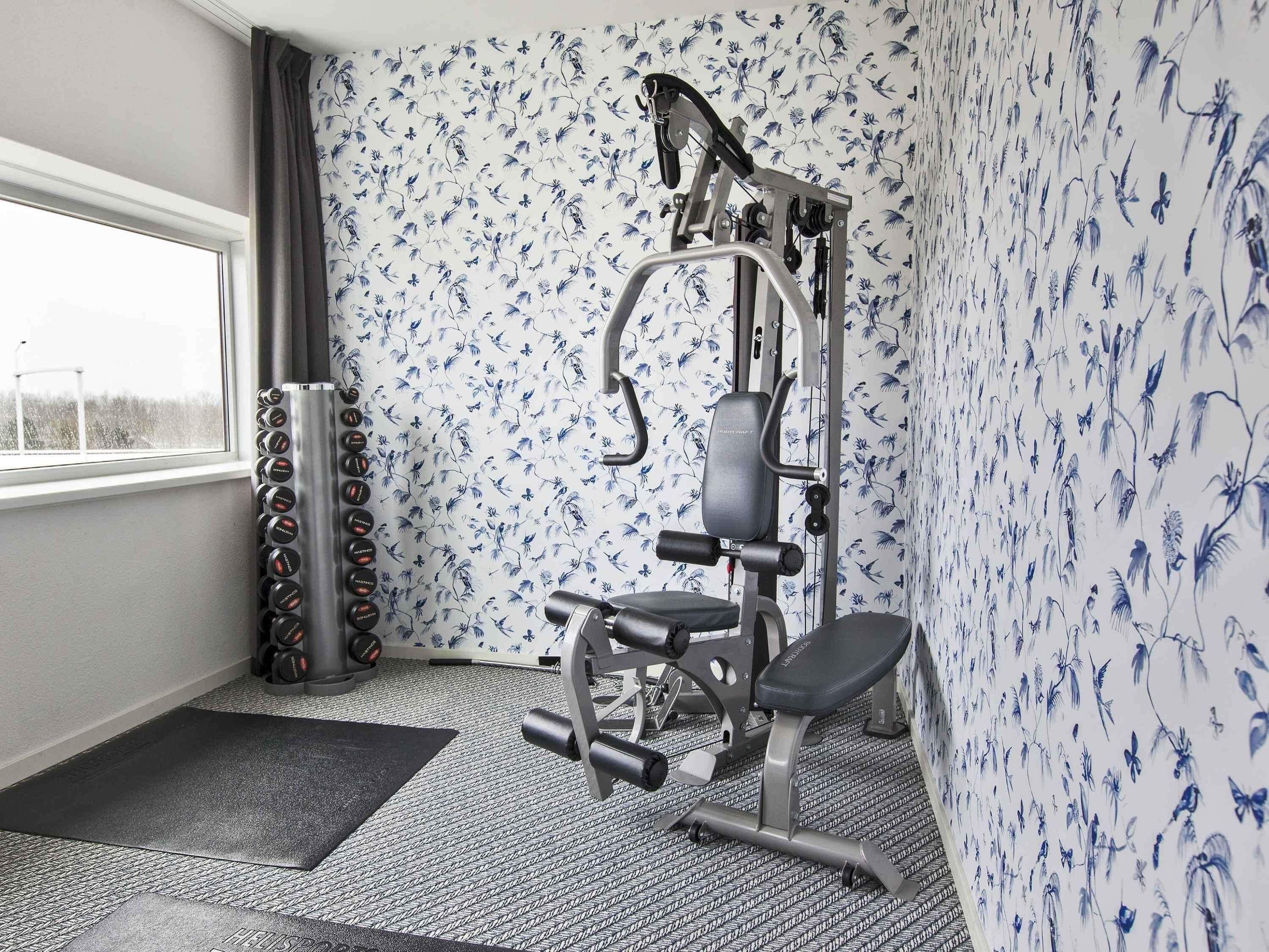A gym with a weight bench, a squat rack, and a wall with floral wallpaper.