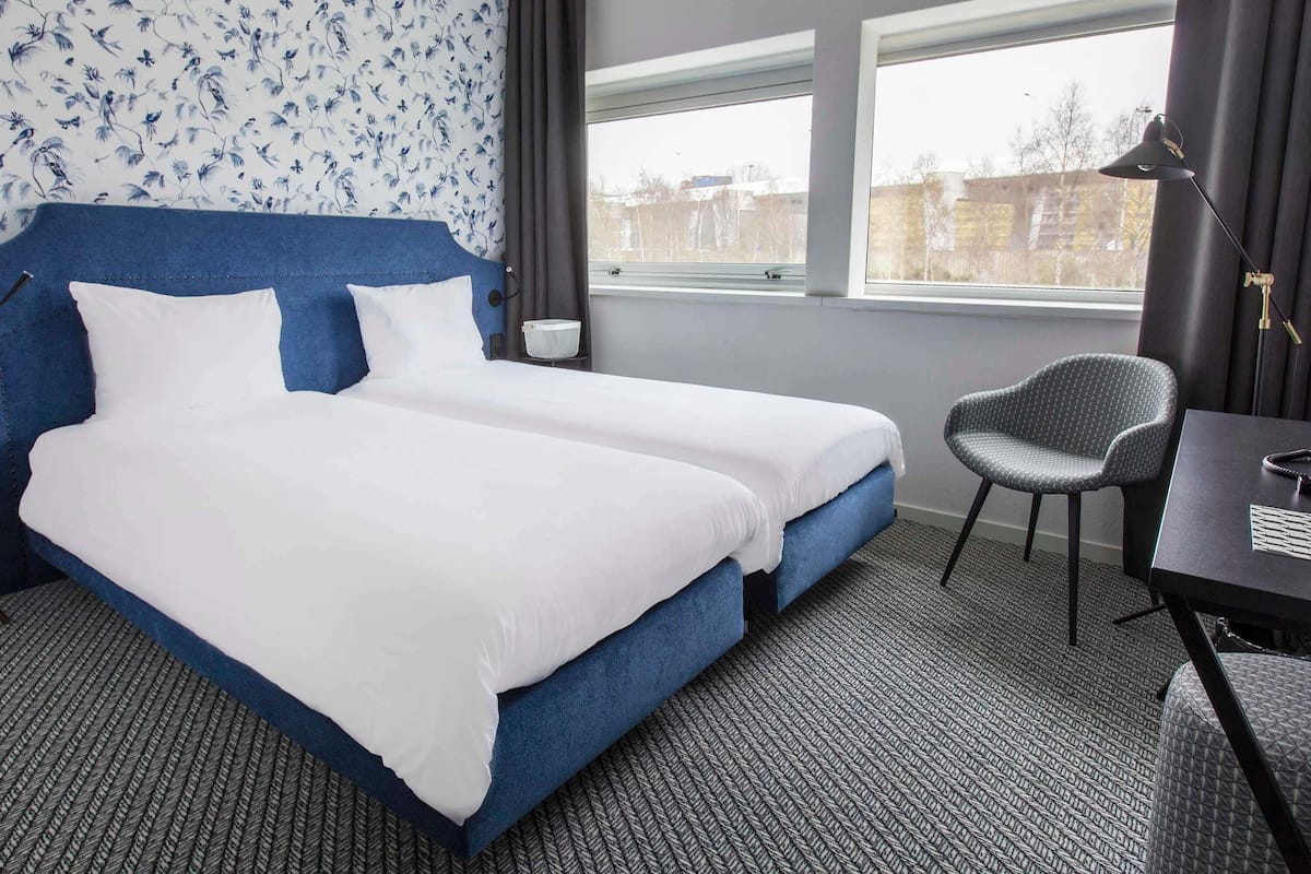 Une chambre d’hôtel avec un grand lit, un bureau, une chaise et une fenêtre donnant sur un beau paysage.