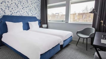 A hotel room with a large bed, a desk, a chair, and a window with a view.