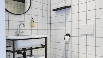 Un baño con un lavamanos blanco, un espejo, un inodoro y un cubo de basura negro.