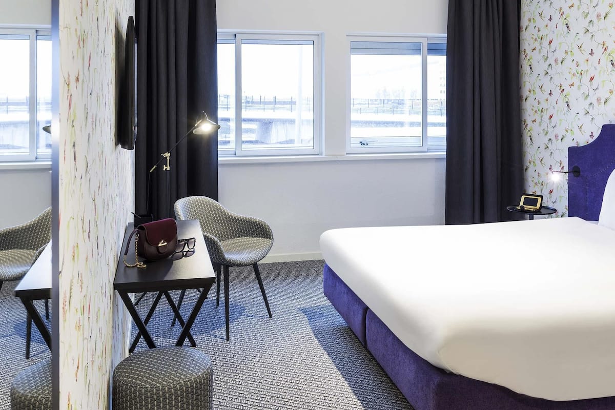 Une chambre d’hôtel avec un lit, deux chaises, un bureau avec une lampe et un téléviseur.