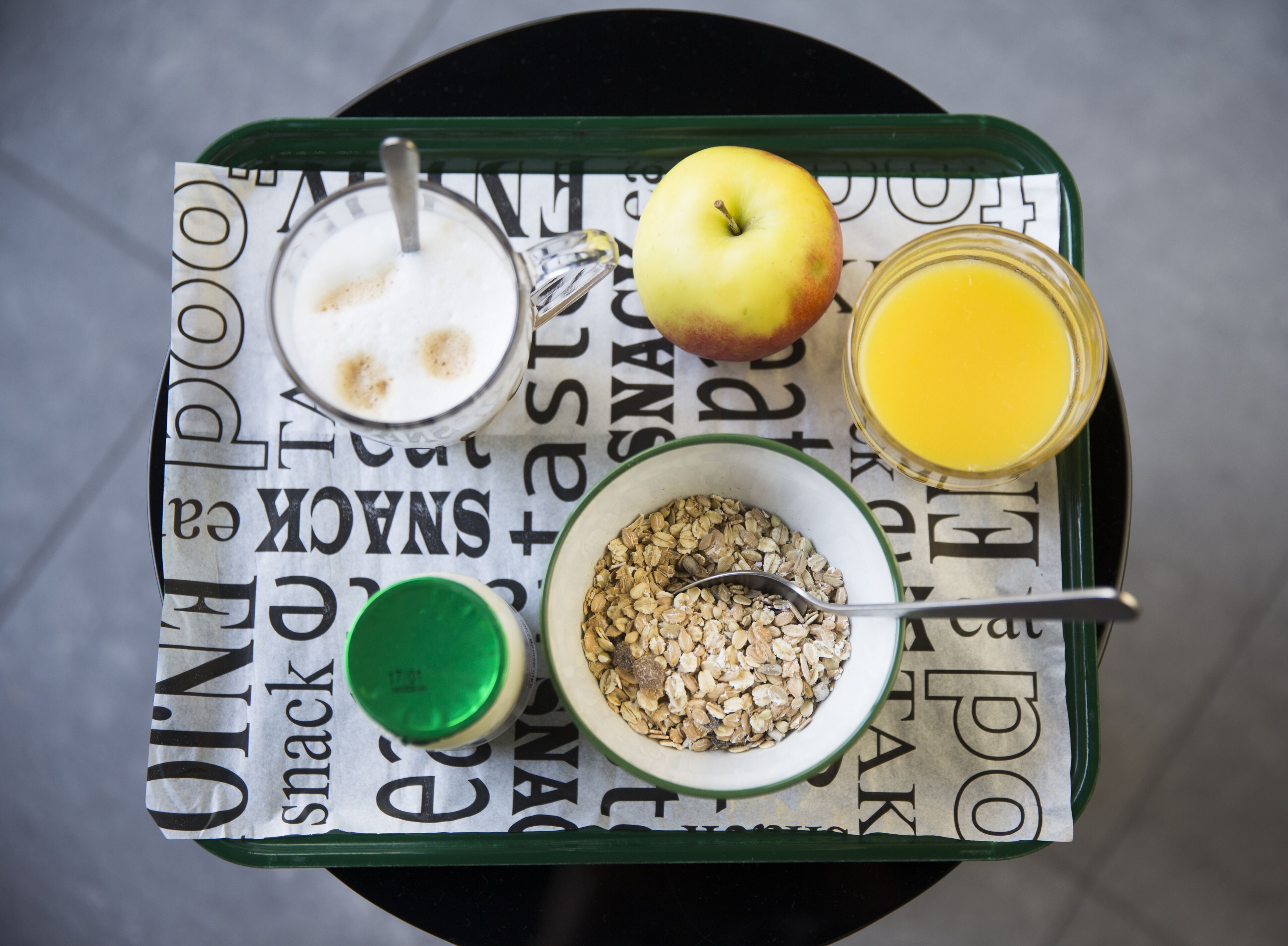 A breakfast tray with a glass of milk, a bowl of cereal, a green drink, an apple, and a glass of orange juice.