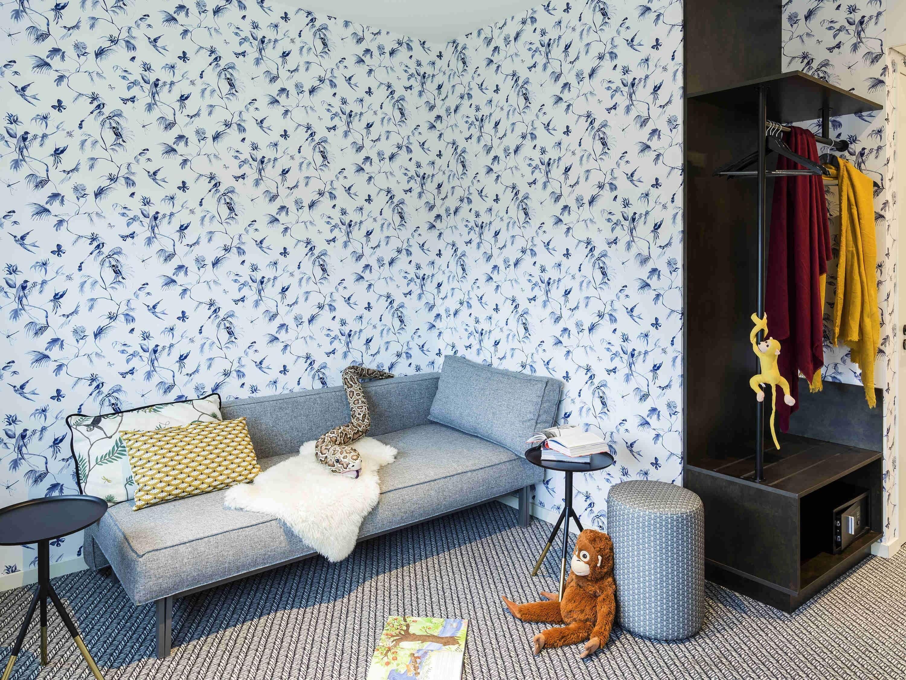 A room with a grey sofa, a small round table, a patterned rug, and a wall with blue floral wallpaper.
