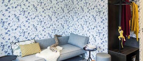 A room with a grey sofa, a small round table, a patterned rug, and a wall with blue floral wallpaper.