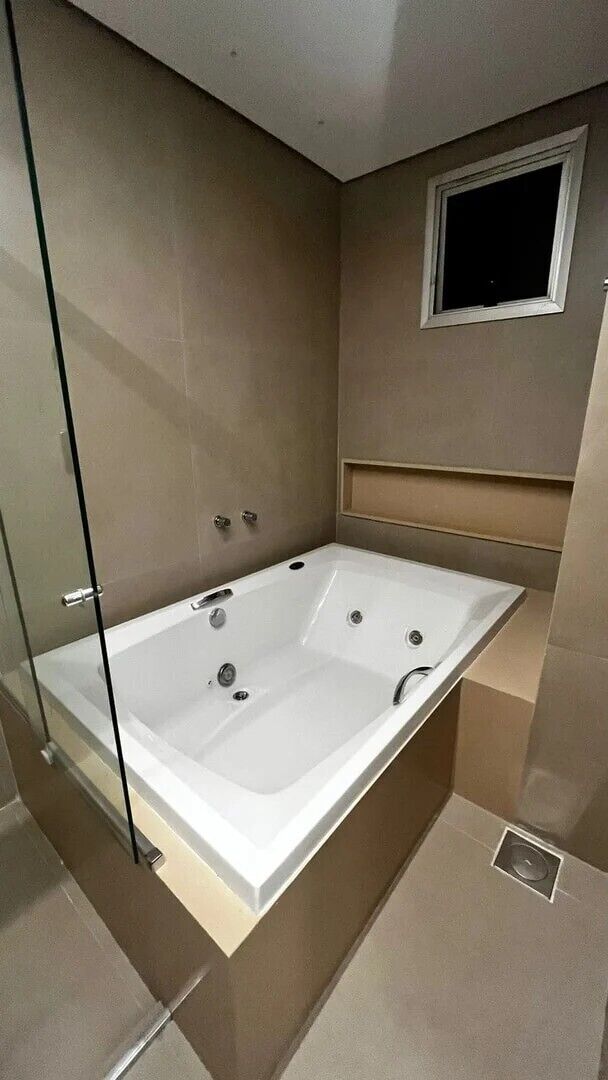 A modern bathroom with a glass-enclosed bathtub, a small window, and a built-in shelf.