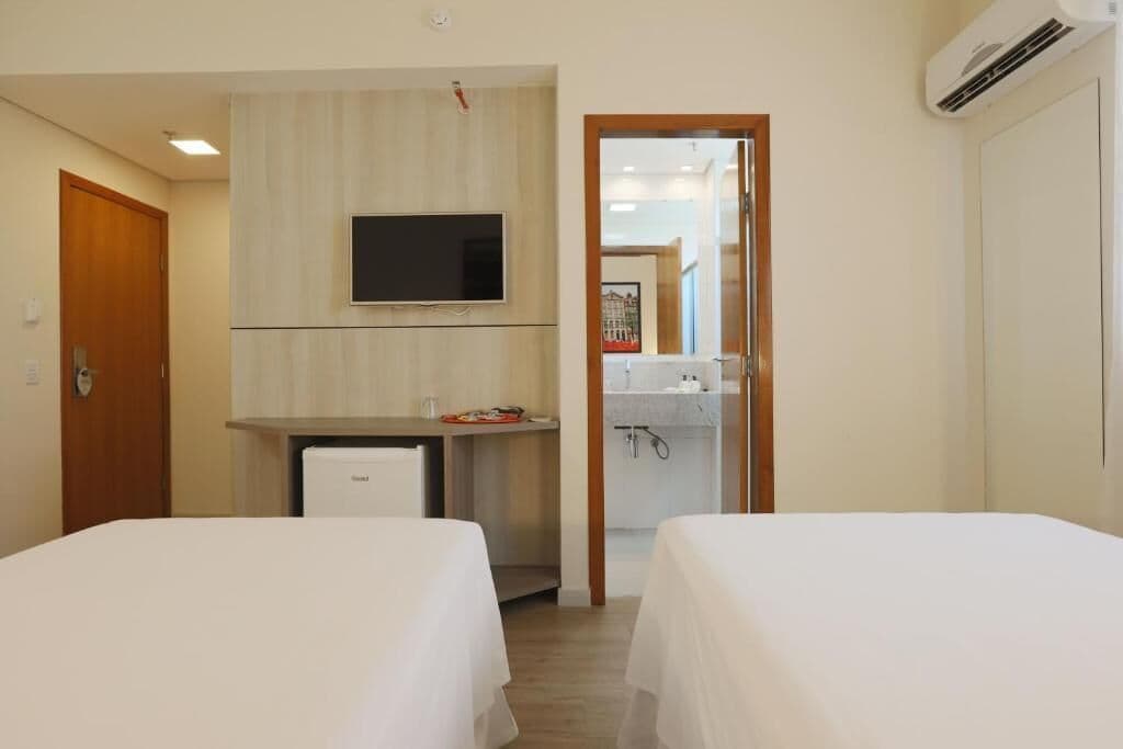 Una habitación de hotel con dos camas, un escritorio con televisor y una kitchenette pequeña.