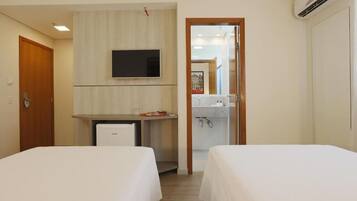 Quarto de hotel com duas camas, uma mesa de trabalho com televisão e uma pequena cozinha.