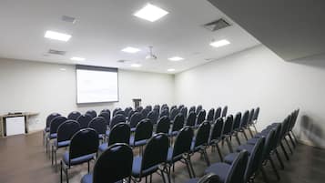 Un salón de conferencias con filas de sillas, una pantalla para proyector y un atril.