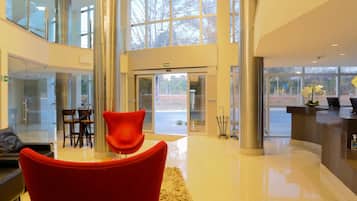 A modern lobby with a reception desk, a chandelier, and a red chair.