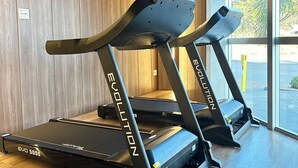 Two Evolution brand treadmills in a modern gym with wooden flooring and large windows. - Hotel Amsterdam Montes Claros (Montes Claros)