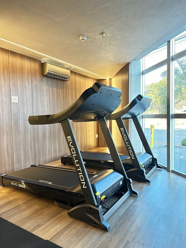 Two Evolution brand treadmills in a modern gym with wooden flooring and large windows. - Hotel Amsterdam Montes Claros (Montes Claros)