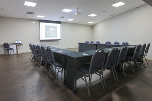 A conference room with a long table, chairs, a projector screen, and a whiteboard. - Hotel Amsterdam Montes Claros (Montes Claros)