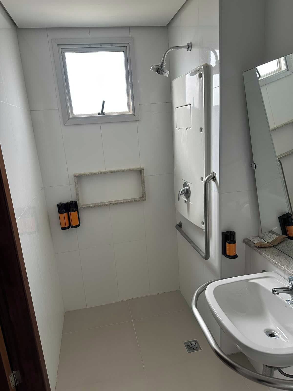 A bathroom with a shower, a sink, a mirror, and a window.