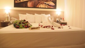 A neatly made bed with white linens, a bouquet of flowers, and rose petals arranged on the bed. - Hotel Amsterdam Montes Claros (Montes Claros)