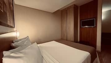 Ein Hotelzimmer mit einem Bett, einem flachbildfernseher an der Wand und einem fenster mit Vorhängen.