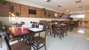 A clean, modern dining area with wooden paneling, multiple tables and chairs, and potted plants. - Hotel Amsterdam Montes Claros (Montes Claros)