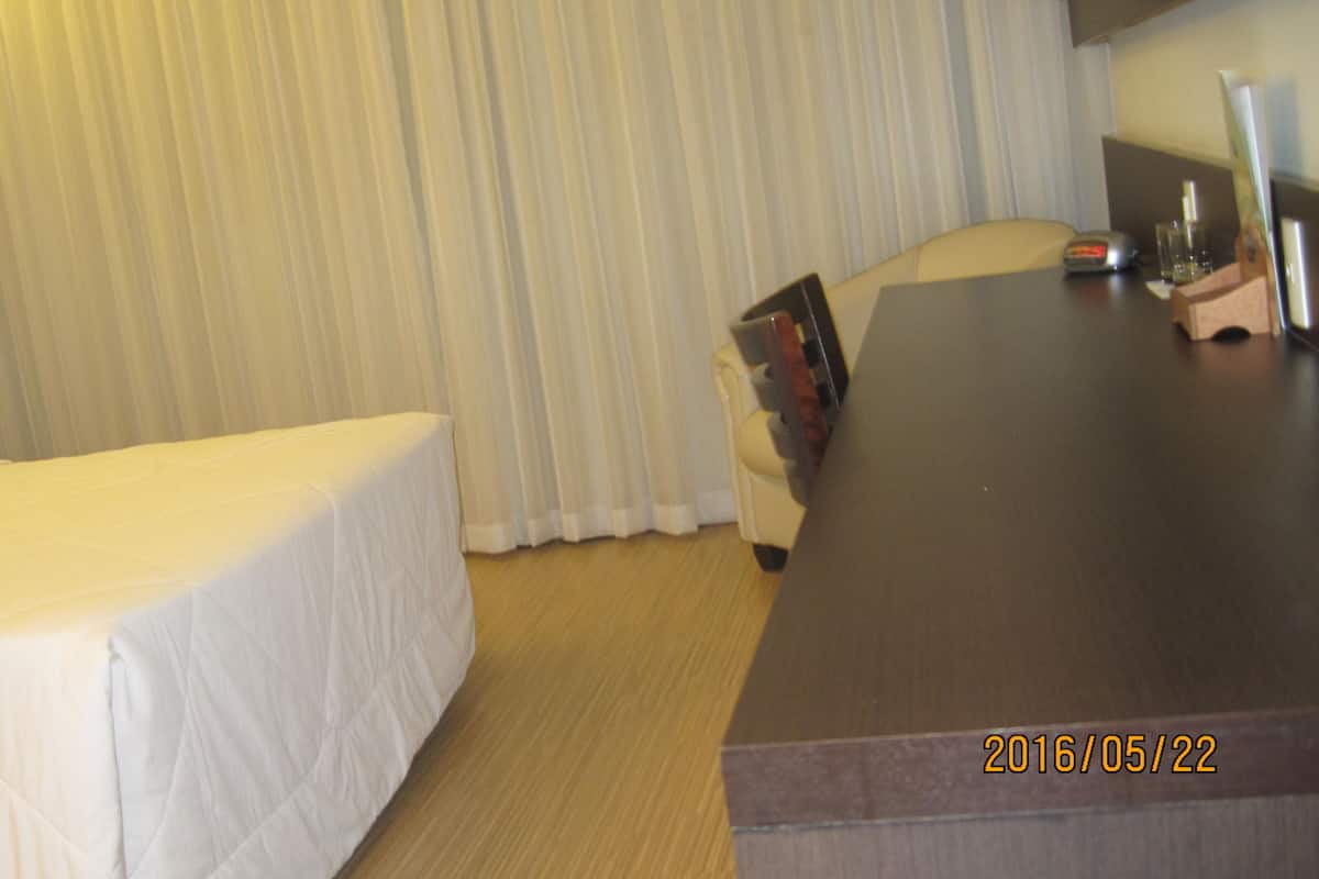 A hotel room with a bed, a desk, a chair, a lamp, and a window with curtains.