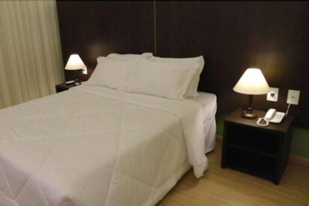 A hotel room with a large bed, two bedside tables with lamps, a telephone, and a curtain.