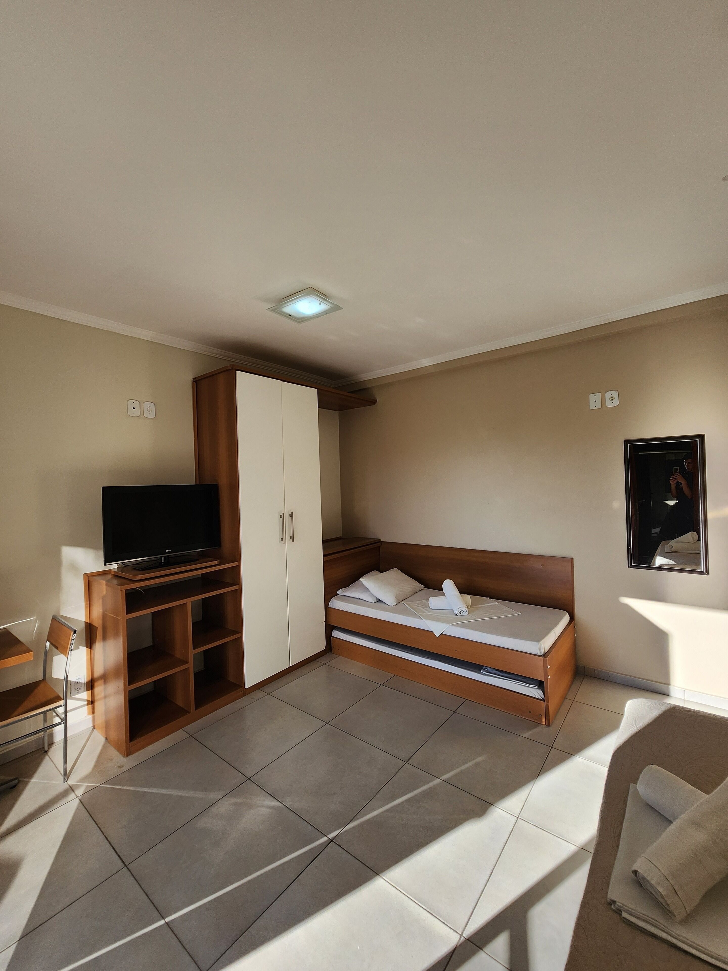 A bedroom with a bed, a TV on a wooden stand, a wardrobe, and a chair.