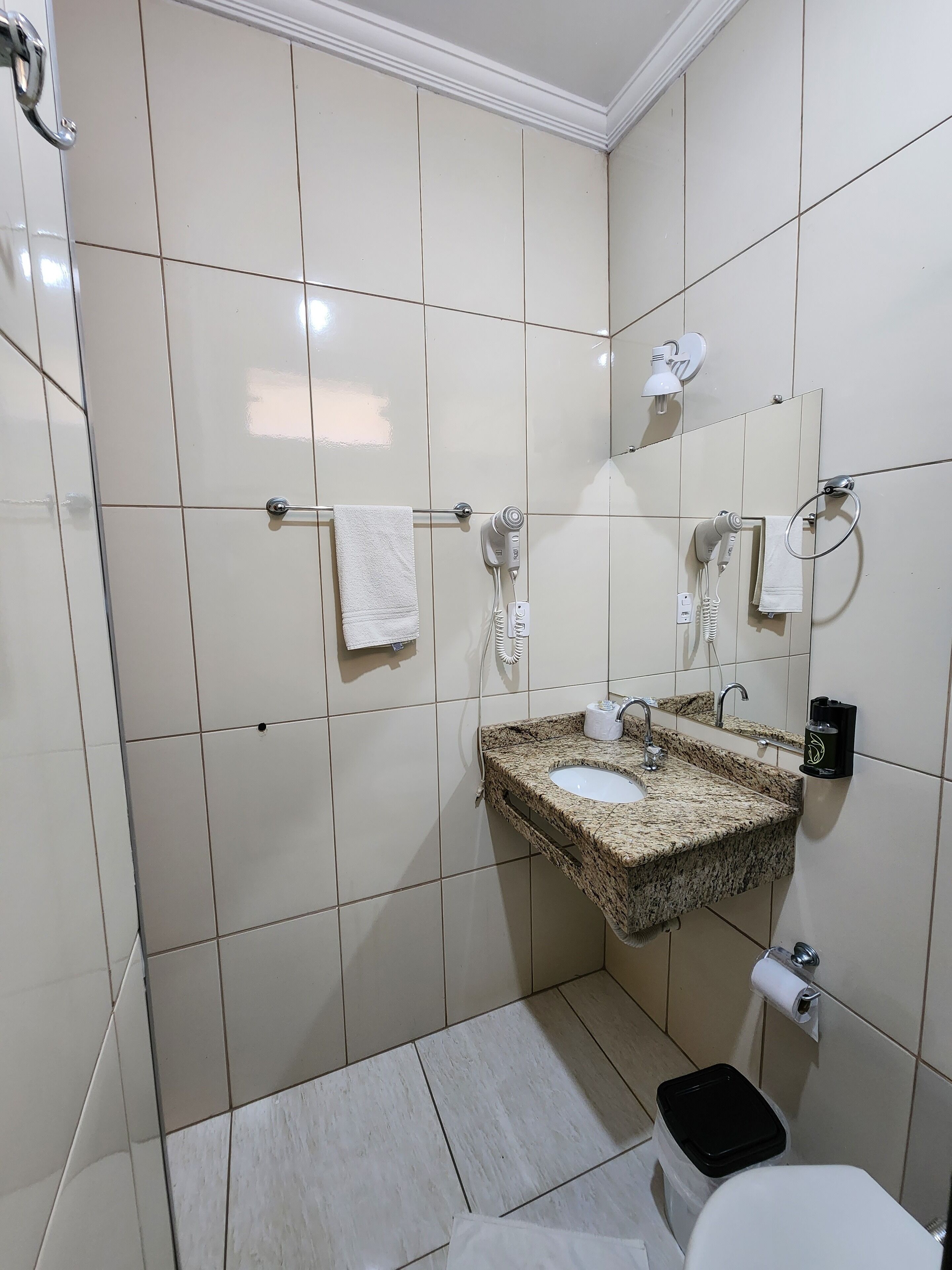 A bathroom with a granite sink, white tiles, a towel rack, a mirror, and a toilet.