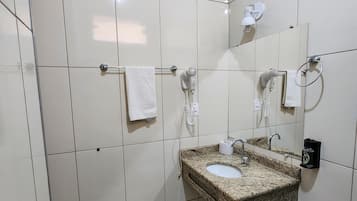 A bathroom with a granite sink, white tiles, a towel rack, a mirror, and a toilet.