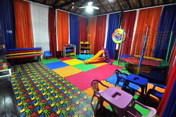 Una sala de juegos con alfombras coloridas, un tobogán y diversas estructuras de juego.