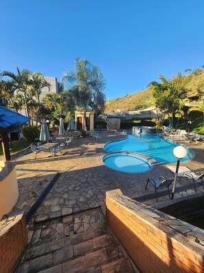 Un área de piscina con dos piscinas, sillas de descanso, sombrillas y un patio de piedra.