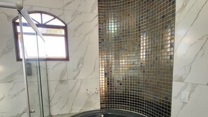 Um banheiro moderno com chuveiro de cabine curvo, porta de vidro e uma grande banheira de hidromassagem preta.