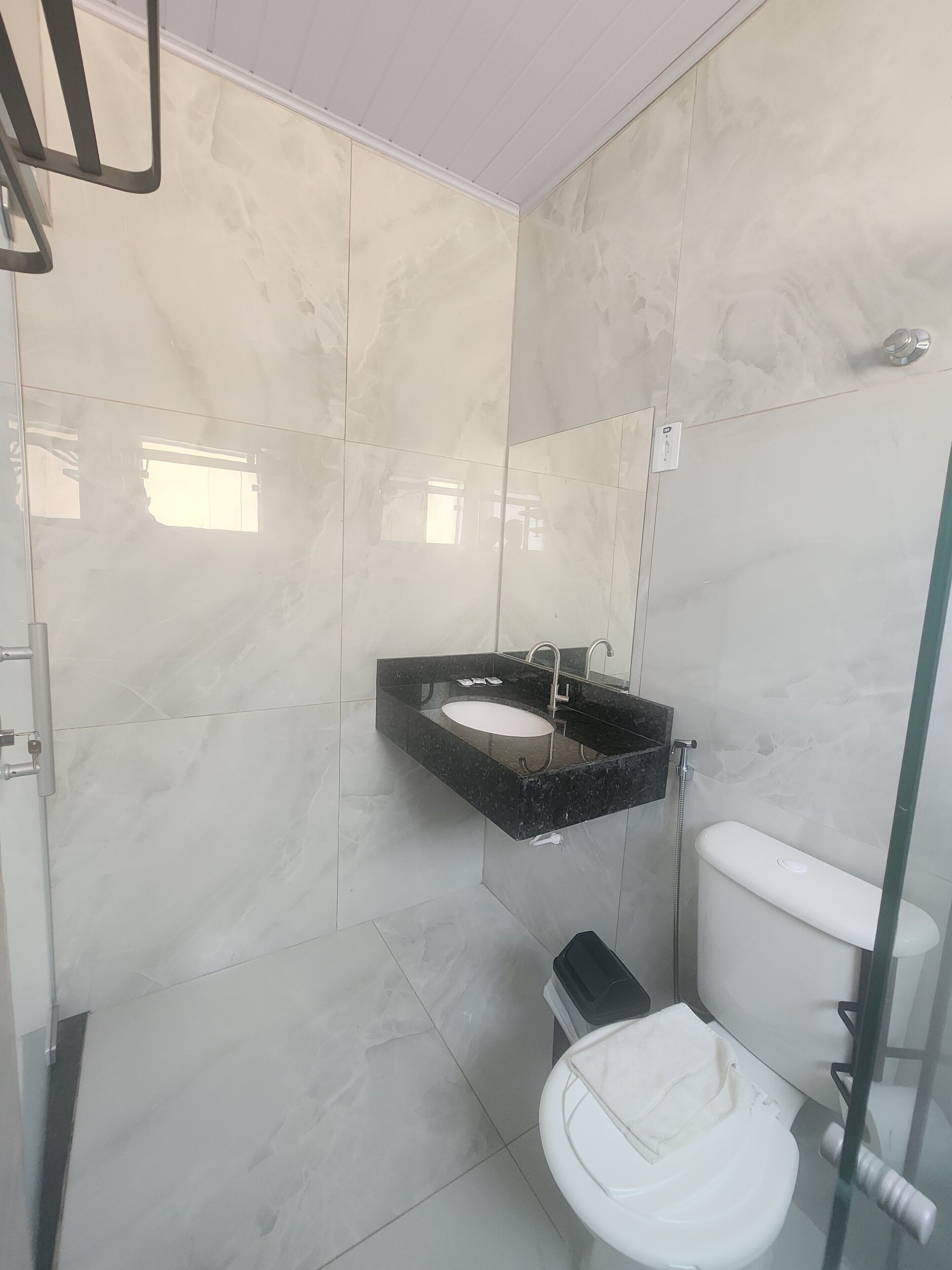 Un baño con inodoro blanco, lavamanos negro y cabina de ducha de vidrio.