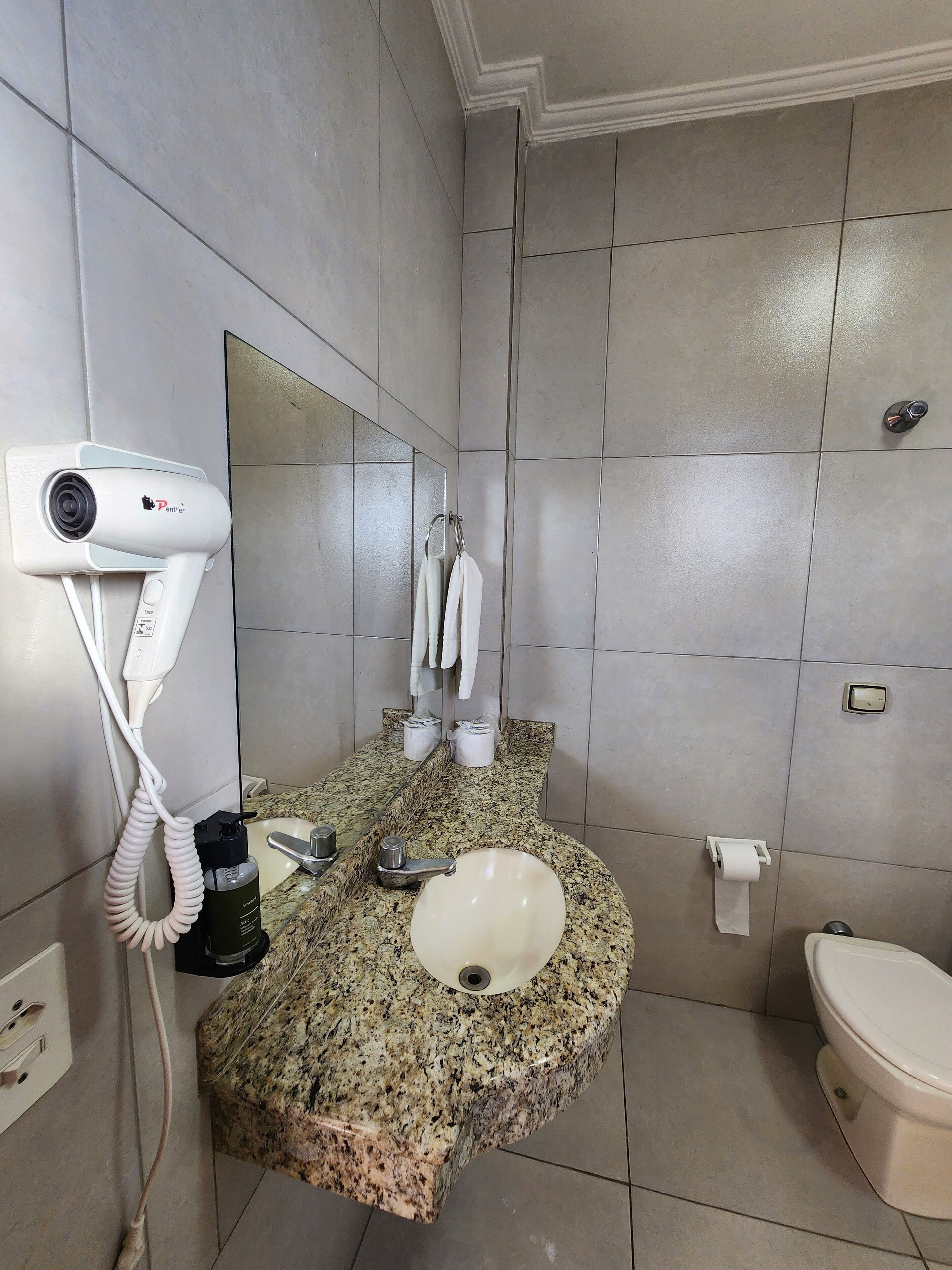 A bathroom with a granite countertop sink, a mirror, a hairdryer, and a toilet.