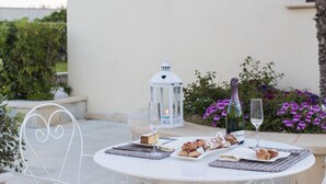 A round outdoor table with a white tablecloth, two wine glasses, a bottle of wine, and a variety of pastries and desserts. - Palascia Wellness Relais (Otranto)