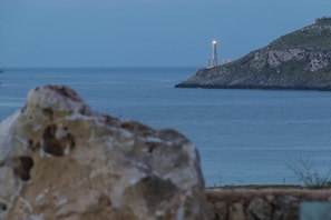 A coastal scene with a lighthouse on a hill, a large rock in the foreground, and calm sea. - Palascia Wellness Relais (Otranto)
