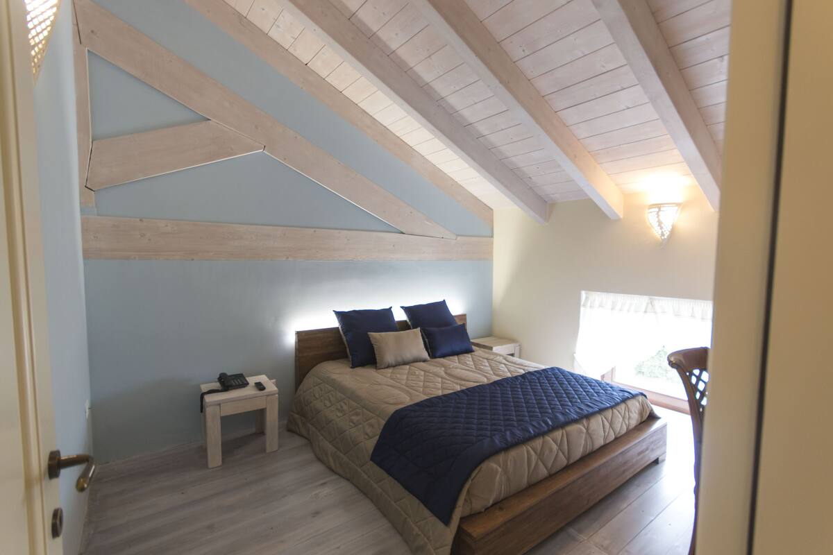 A bedroom with a wooden ceiling, a bed with a quilted cover, two bedside tables, and a nightstand.