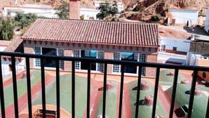 A building with a tiled roof, surrounded by a fenced courtyard with a green and red patterned floor. - Hostal Rural Gloria (Cortes y Graena)