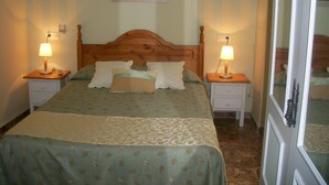 A neatly made bed with a patterned bedspread, two bedside tables with lamps, and a painting on the wall above the bed. - Hostal Rural Gloria (Cortes y Graena)