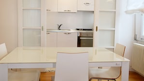 Cocina compacta con armarios blancos, un lavamanos y una estufa. En primer plano, hay una mesa de comedor con sillas.